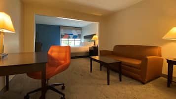 A hotel room with a bed, a desk, an orange chair, a brown sofa, and two lamps.