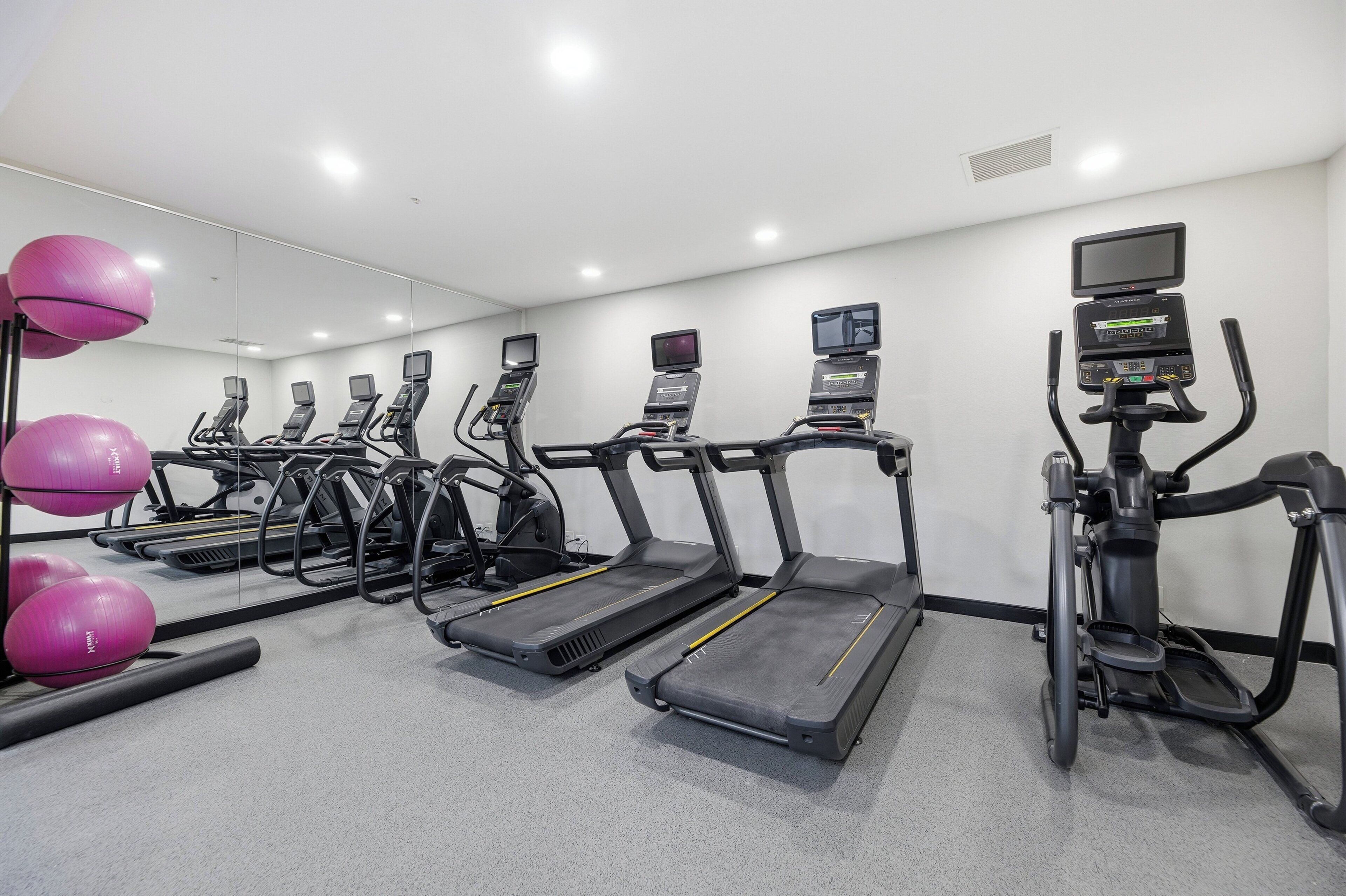 A gym with multiple treadmills, exercise balls, and a mirrored wall.