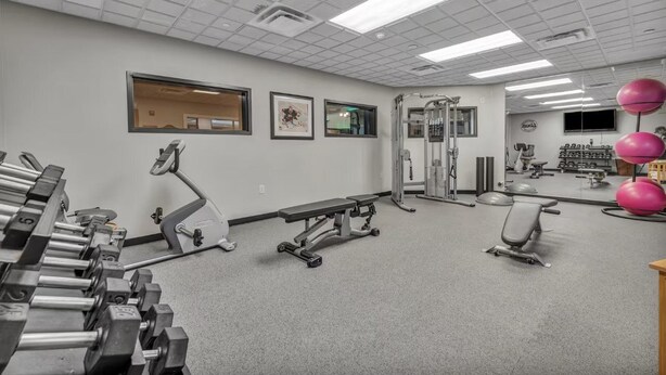 A gym with exercise equipment, a bench, and a wall-mounted television. - Holiday Inn Express & Suites RALEIGH WEST - LENOVO CENTER by IHG (Meredith)