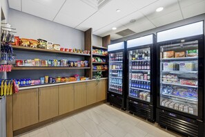 A snack and beverage vending area with multiple shelves stocked with various snacks and drinks, and two refrigerated beverage dispensers. - Holiday Inn Express & Suites RALEIGH WEST - LENOVO CENTER by IHG (Meredith)