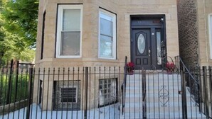 A two-story building with a dark front door, a brick facade, and a metal fence in front.