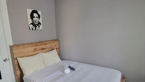 A neatly made bed with a wooden headboard, a pillow, and a rolled towel on a plain wall with a single piece of artwork.
