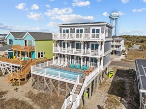 A multi-story beach house with a pool, deck chairs, and a water tower in the background. - Clear Skies: Spacious 7-Bedroom Oceanfront Retreat in Oak Island, NC, perfect for up to 20 guests. (Oak Island)