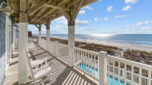 A wooden deck with a pool, overlooking a beach and ocean. - Clear Skies: Spacious 7-Bedroom Oceanfront Retreat in Oak Island, NC, perfect for up to 20 guests. (Oak Island)