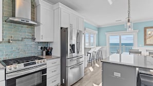 A modern kitchen with stainless steel appliances, white cabinetry, and a view to the outside. - Clear Skies: Spacious 7-Bedroom Oceanfront Retreat in Oak Island, NC, perfect for up to 20 guests. (Oak Island)