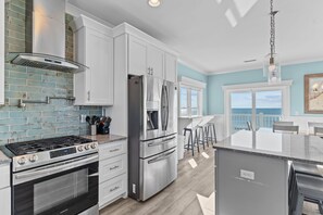 A modern kitchen with stainless steel appliances, white cabinetry, and a view to the outside. - Clear Skies: Spacious 7-Bedroom Oceanfront Retreat in Oak Island, NC, perfect for up to 20 guests. (Oak Island)