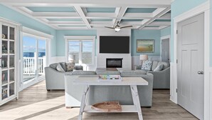 A spacious living room with a fireplace, a sofa, and a dining table. - Clear Skies: Spacious 7-Bedroom Oceanfront Retreat in Oak Island, NC, perfect for up to 20 guests. (Oak Island)