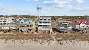 A beachfront property with a water tower, multiple houses, and a sandy beach. - Clear Skies: Spacious 7-Bedroom Oceanfront Retreat in Oak Island, NC, perfect for up to 20 guests. (Oak Island)