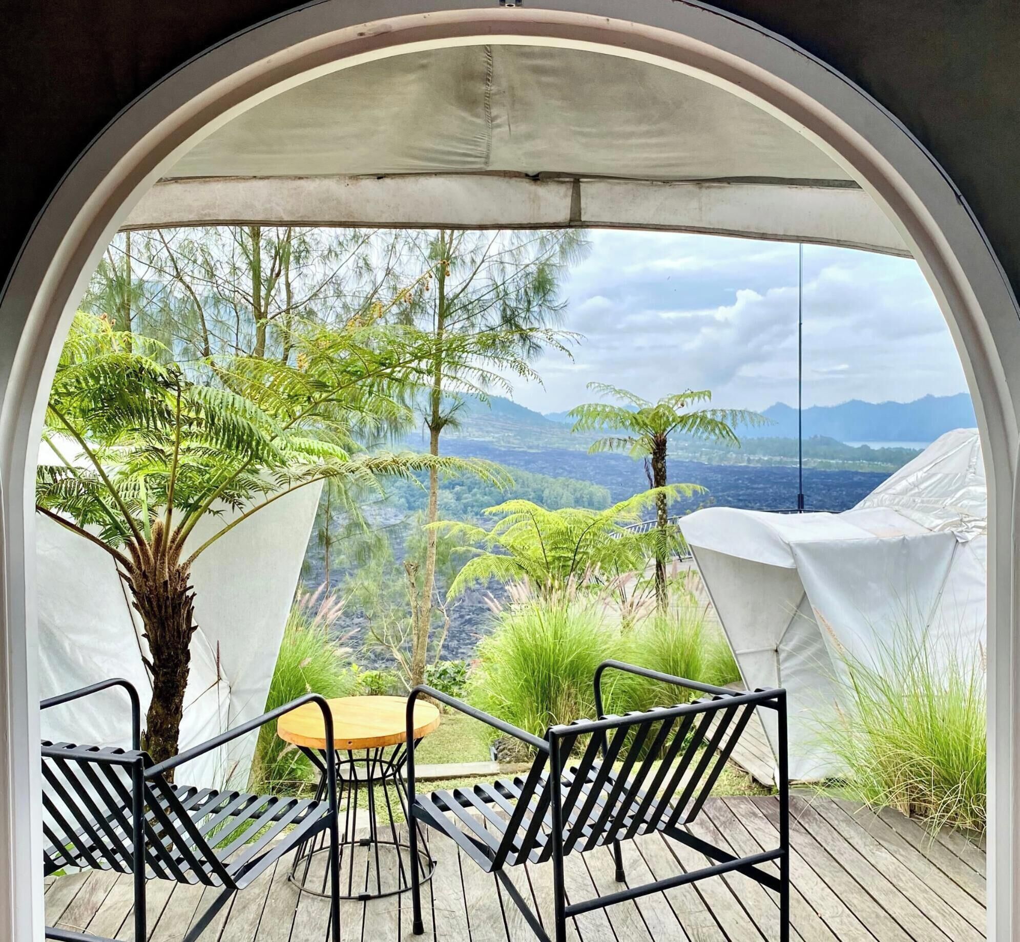 Un espacio al aire libre techado con mesa y sillas, rodeado de follaje y una vista panorámica.