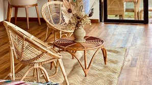 A room with wicker furniture, a curtain, a wall art piece, and a view through a glass door. - Black Lava Camp Kintamani (Kintamani)