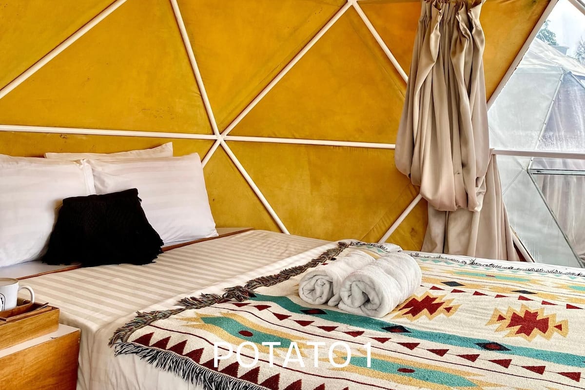 Una habitación con diseño geométrico en la pared, amarillo y blanco, una cama con ropa de cama blanca, una toalla enrollada y una ventana con cortinas.