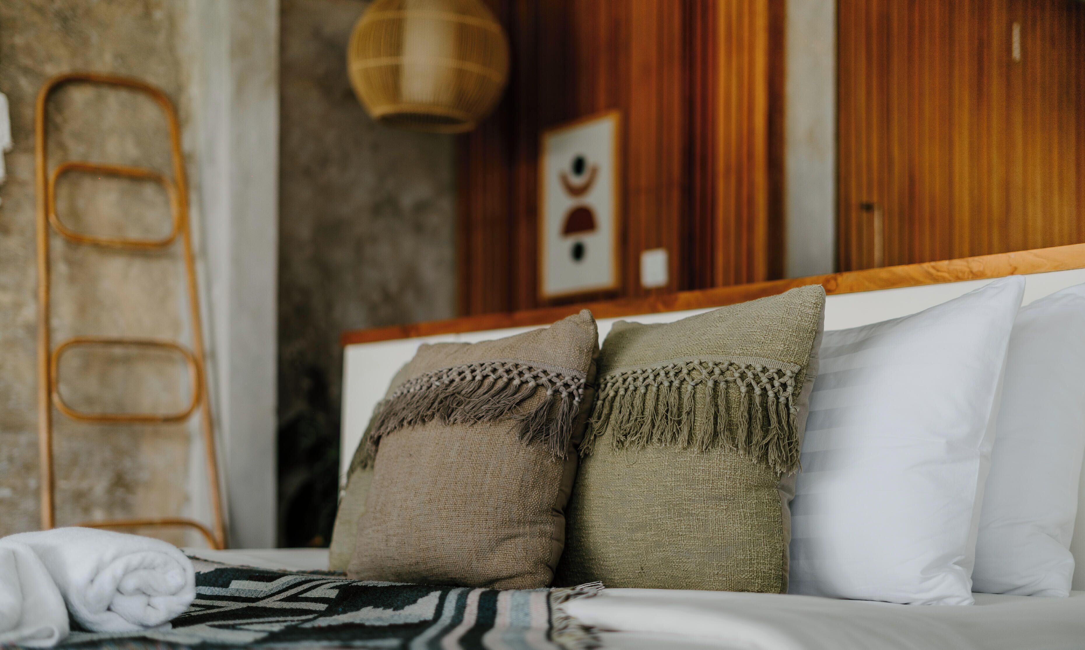 A bed with two textured pillows, a white pillow, and a rolled white towel.