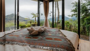 A bedroom with a large bed, a patterned rug, and a view of greenery and mountains. - Black Lava Camp Kintamani (Kintamani)