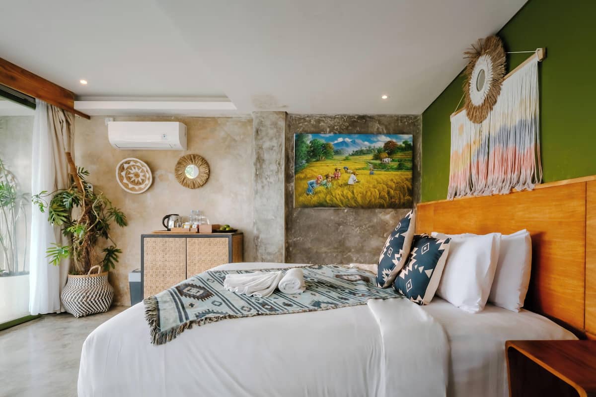 Un dormitorio con una cama, una mesita de noche, un aire acondicionado instalado en la pared, un cuadro y una pared verde.