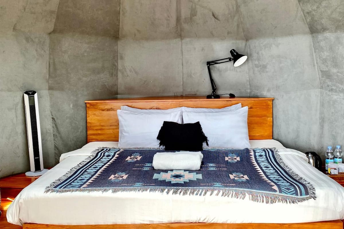 Un dormitorio con cabecera de madera, cama con colcha estampada, lámpara de noche y calentador fijado a la pared.