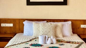 Una cama con una manta estampada, almohadas blancas y una obra enmarcada en la pared.