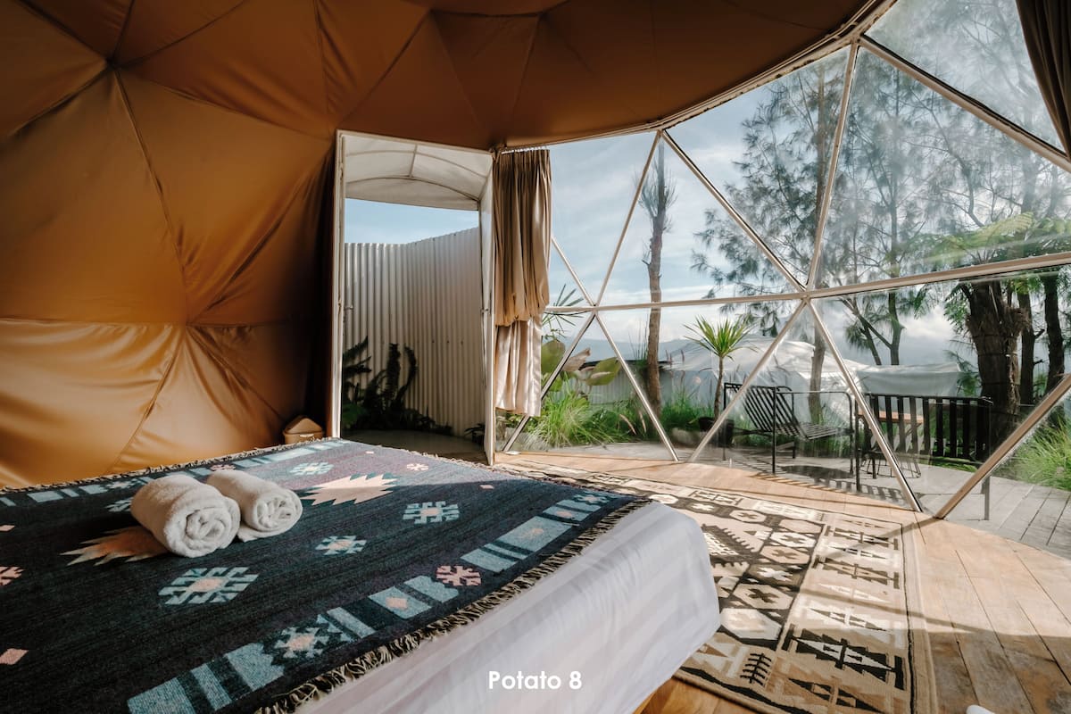 Una habitación tipo tienda de campaña acogedora, con una cama, vistas al exterior y una ventana con cortinas.