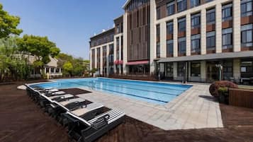 A modern hotel with a swimming pool, lounge area, and a multi-story building with large windows.