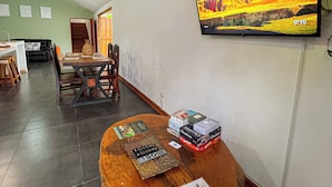 Un vestíbulo de hotel con una mesa de madera que exhibe libros y controles remotos, un televisor montado en la pared y una escalera que lleva a otra zona.