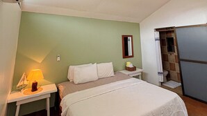 Un dormitorio con cama, mesita de noche, lámpara, ventilador de techo y un baño pequeño con ducha.