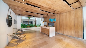 Un espace d’accueil moderne avec un comptoir en bois, une lampe suspendue et un coin salon avec des chaises à rayures.