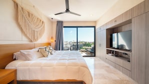 Une chambre d’hôtel moderne dotée d’un grand lit, d’un ventilateur de plafond, d’un téléviseur posé sur une commode en bois et offrant une vue sur la ville grâce à de grandes fenêtres.