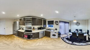 Uma cozinha compacta com forno embutido, micro-ondas e pia, uma área de refeições com mesa e cadeiras, e uma lavanderia com máquina de lavar.
