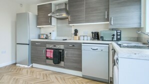 Uma cozinha moderna com armários cinza, forno embutido, lava-louças e uma pia de aço inoxidável.