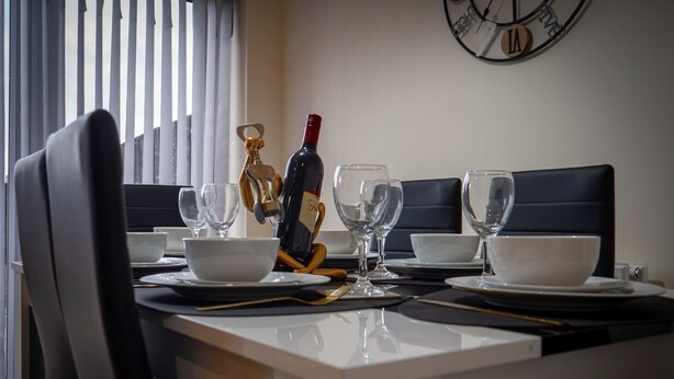 Uma mesa de jantar posta com pratos, tigelas e copos de vinho brancos, uma garrafa de vinho e um chaveiro dourado.