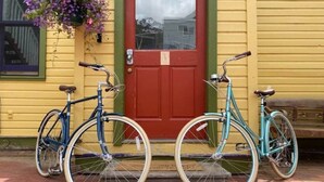 Duas bicicletas estacionadas em frente a um prédio amarelo com uma porta vermelha.