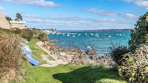 A coastal view with boats, rocky shore, and a building with a modern design.