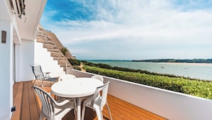 A balcony with a wooden deck, white plastic chairs, and a round table.