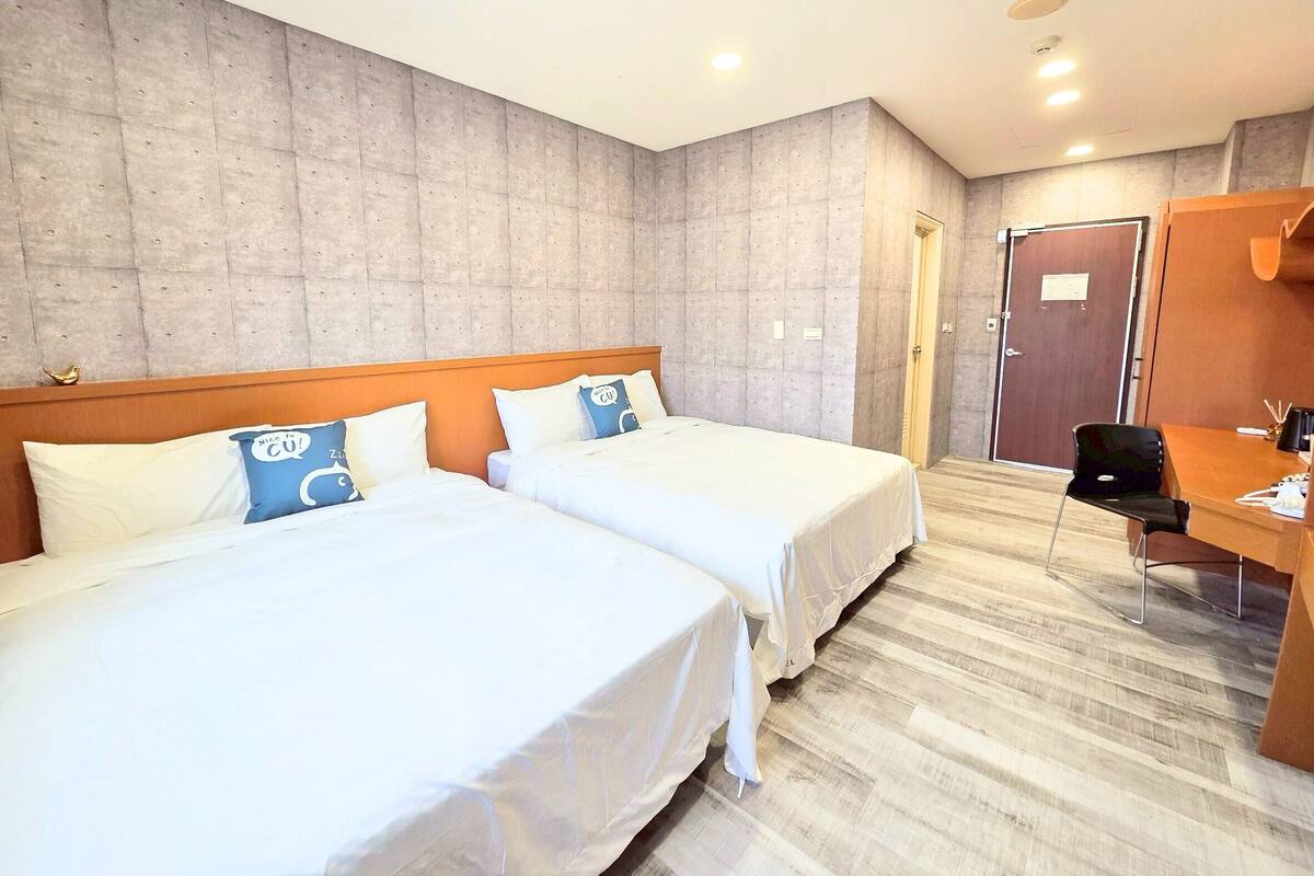 Habitación de hotel con dos camas, un escritorio y una puerta.