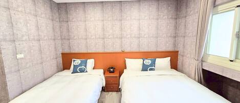 Habitación de hotel con dos camas individuales, cabecera de madera, mesita de noche con teléfono y ventana con cortinas.