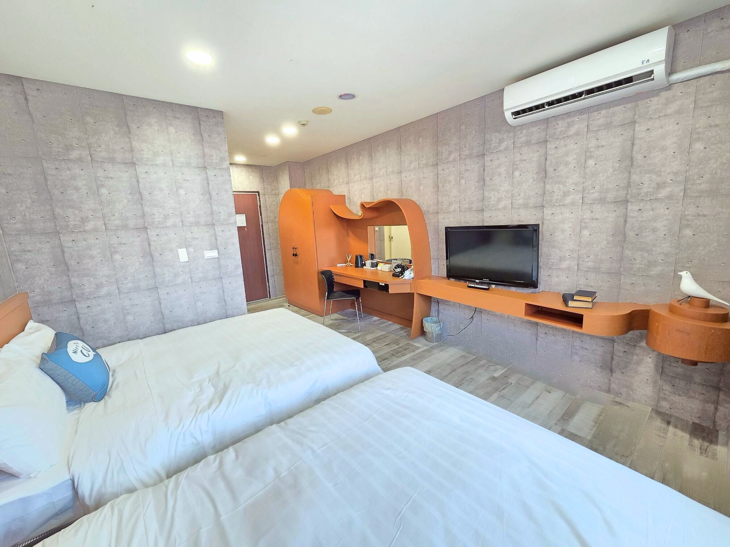 Habitación de hotel con dos camas, un escritorio con televisor y aire acondicionado.