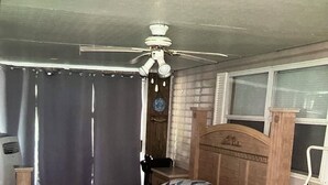 Ein Schlafzimmer mit einem Holzbett, einem Nachttisch, einer Kommode, einem Deckenventilator und einem Fenster mit Jalousien.