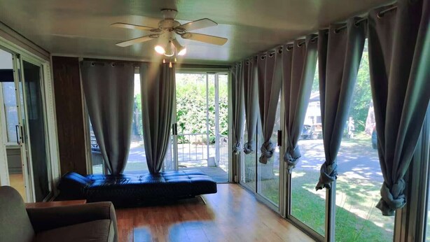 Ein Zimmer mit einer großen Schiebeglastür, einem Deckenventilator und einem schwarzen Sofa.