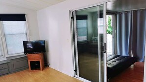 Ein Zimmer mit einer Schiebeglas-Tür, einem Fernseher auf einer Holzkommode und einem Fenster mit Jalousien.