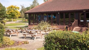 A covered pavilion with a tiled roof, surrounded by picnic tables and greenery. - Holiday Inn COLCHESTER by IHG (Eight Ash Green)
