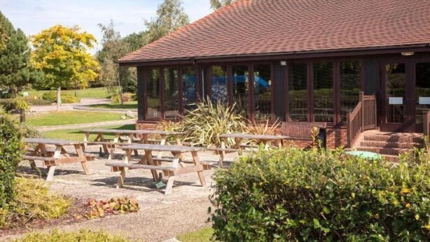 A covered pavilion with a tiled roof, surrounded by picnic tables and greenery. - Holiday Inn COLCHESTER by IHG (Eight Ash Green)