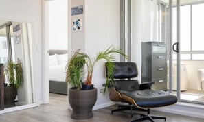Ein modernes Wohnzimmer mit einem großen Fenster, einem schwarzen Ledersessel, einer Korbmöbellampe und einem Bett im Hintergrund.