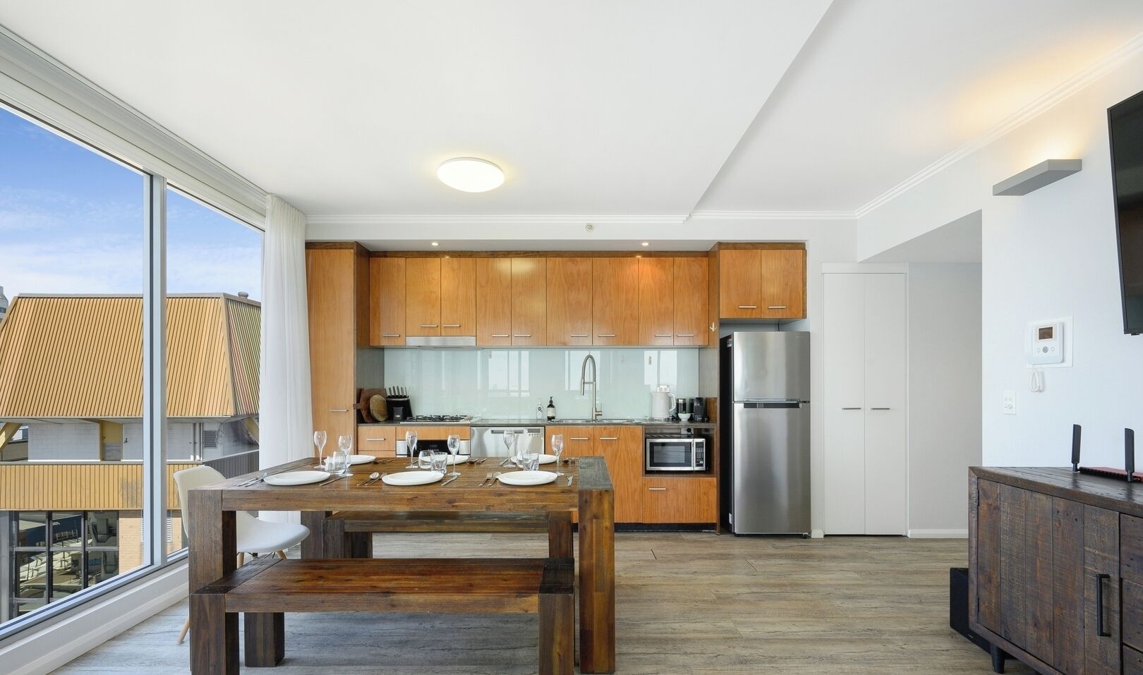 A modern kitchen with wooden cabinets, stainless steel appliances, and a dining area with a wooden table set for four.