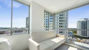 En balkong med en soffa, stora fönster och utsikt över höga byggnader.