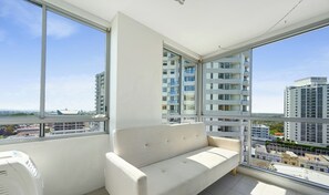 Ein Balkon mit einer Sitzecke, großen Fenstern und Blick auf hohe Gebäude.