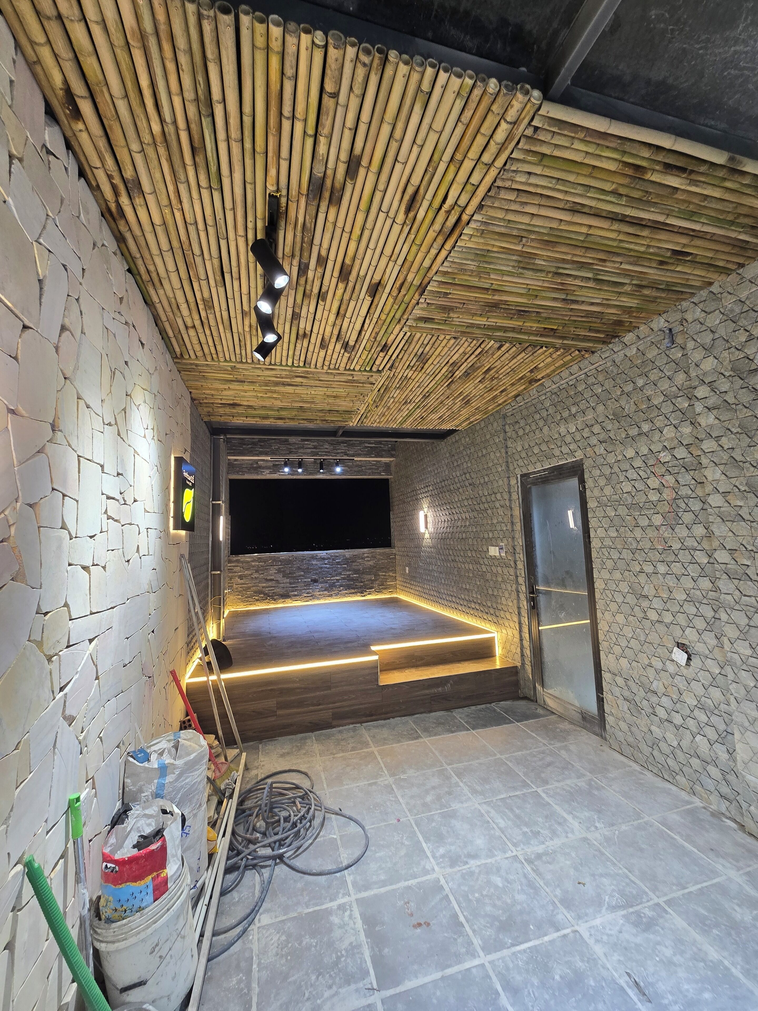 A room with a bamboo ceiling, stone walls, a flat-screen TV, and a door.