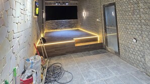 Een kamer met een bamboe plafond, stenen muren, een flatscreentelevisie en een deur.