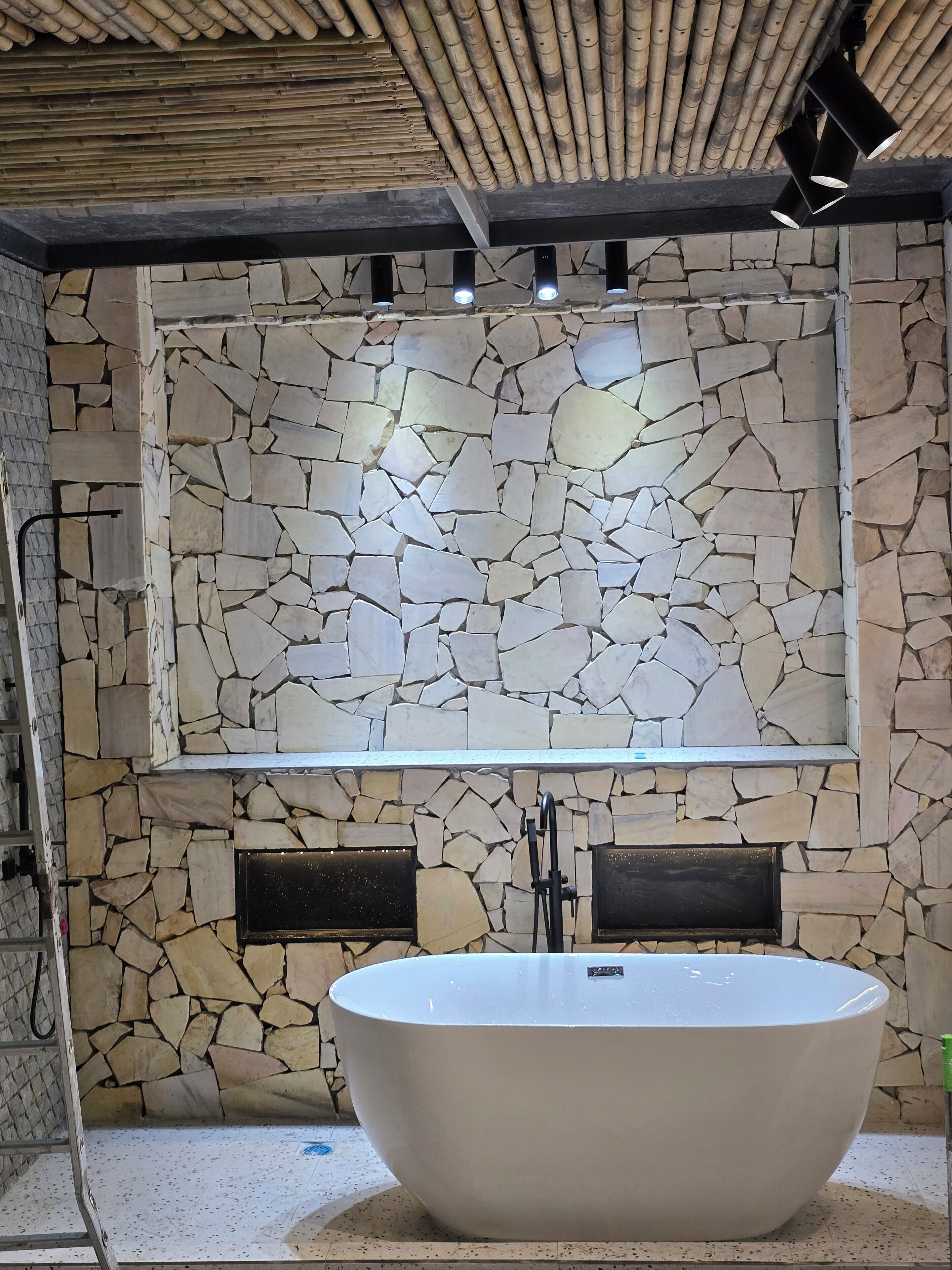 A bathroom with a stone mosaic wall, a freestanding bathtub, and a bamboo ceiling.