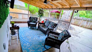 Un patio couvert aménagé avec des meubles en osier, un tapis à motifs bleus et un plafond en bois.