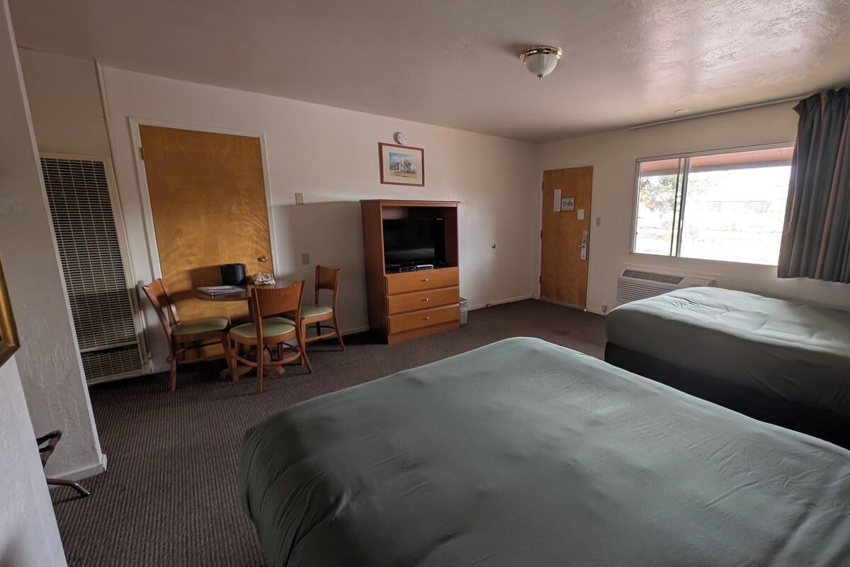 Hotellihuone, jossa on kaksi sänky ä, työpöytä tuolilla, televisio ja ikkuna, jossa on verhot.