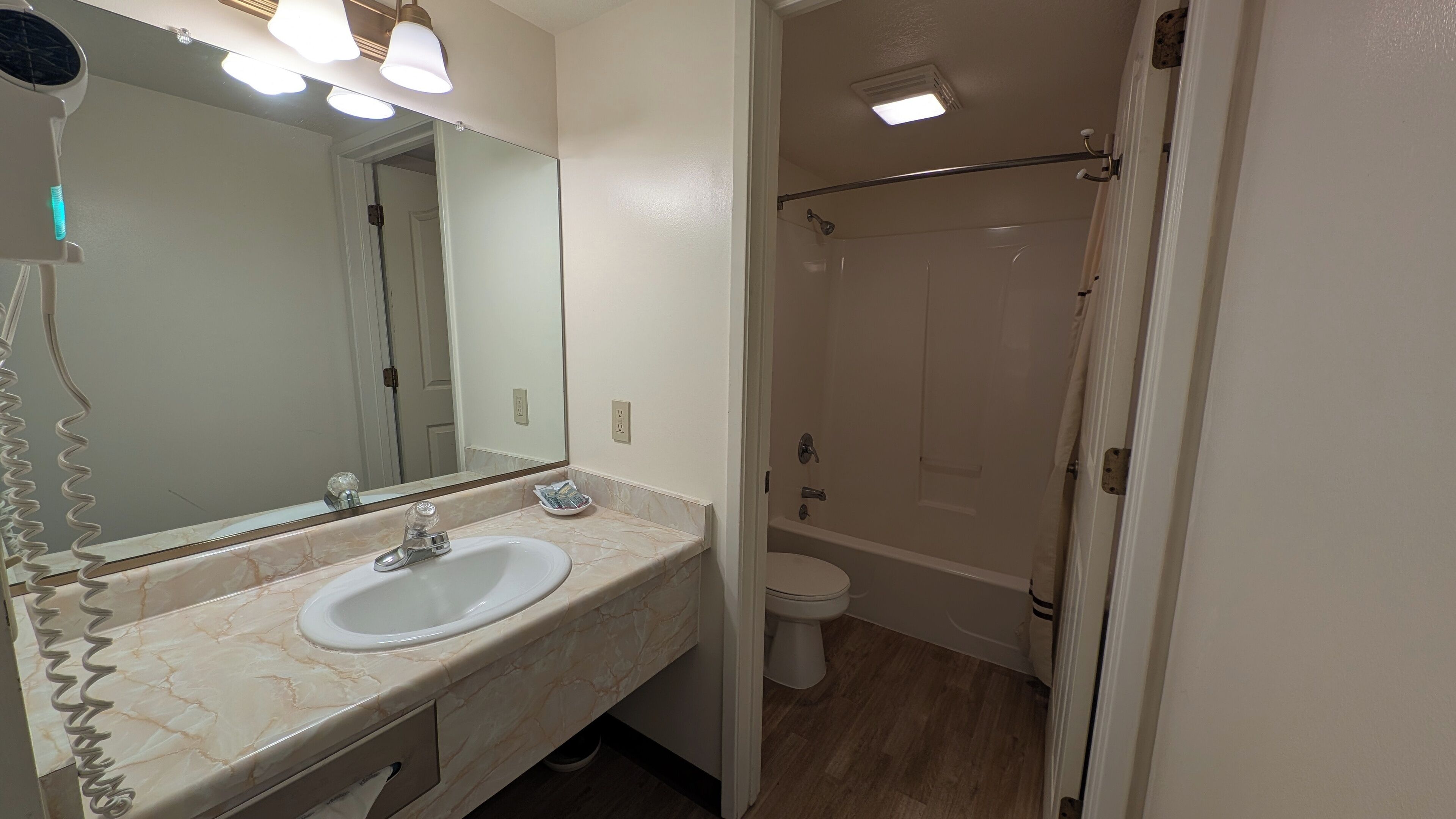A bathroom with a marble vanity, a large mirror, a shower, and a toilet.